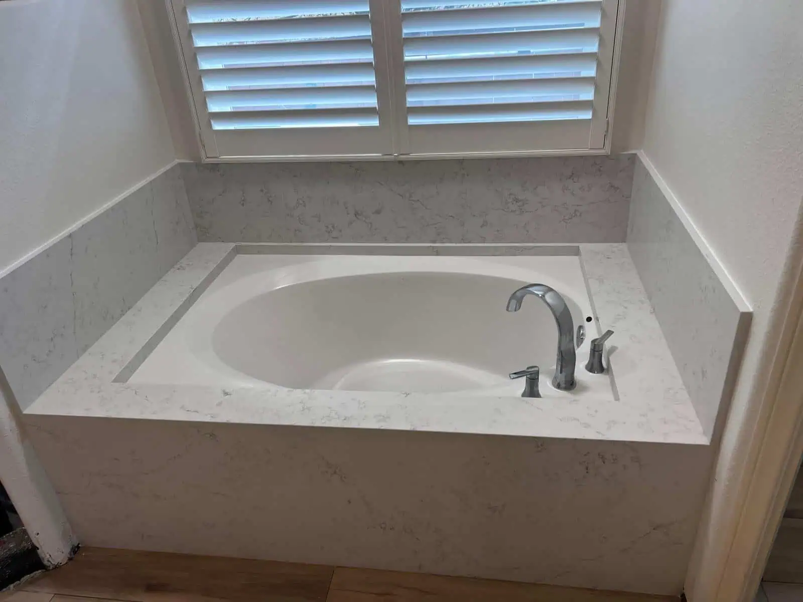 Luxury bathtub with stone slab surround and window shutters in bathroom.