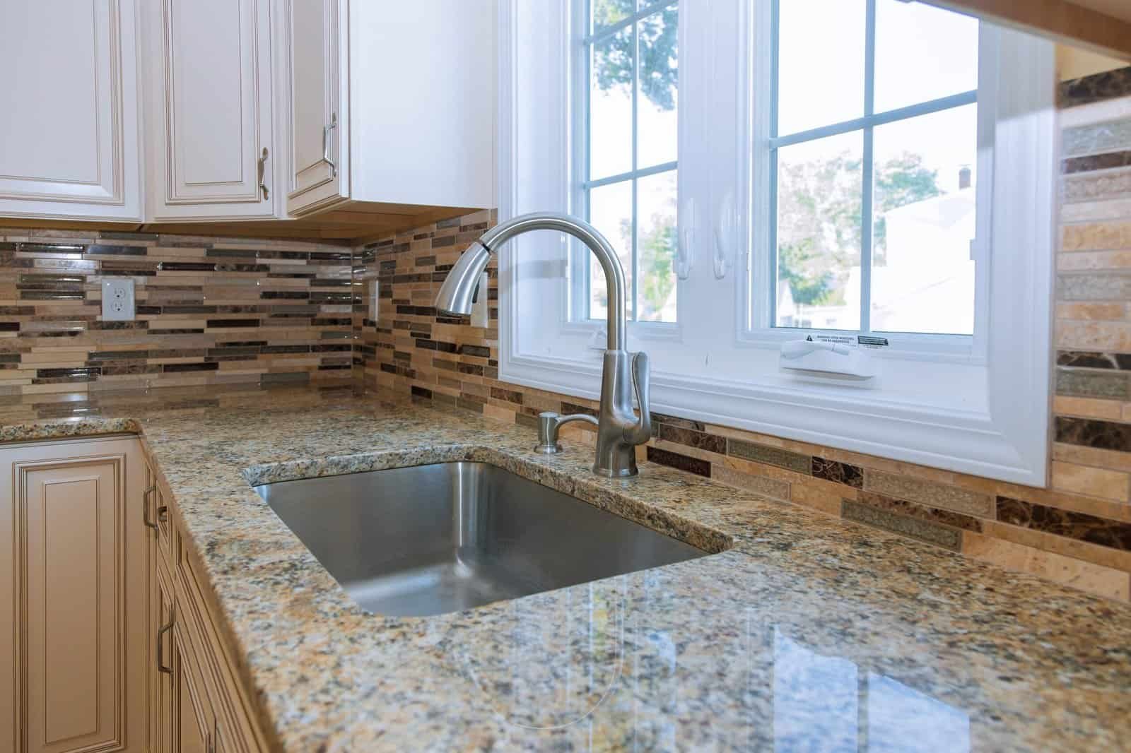 Close-up of granite kitchen countertop with sink and window view.