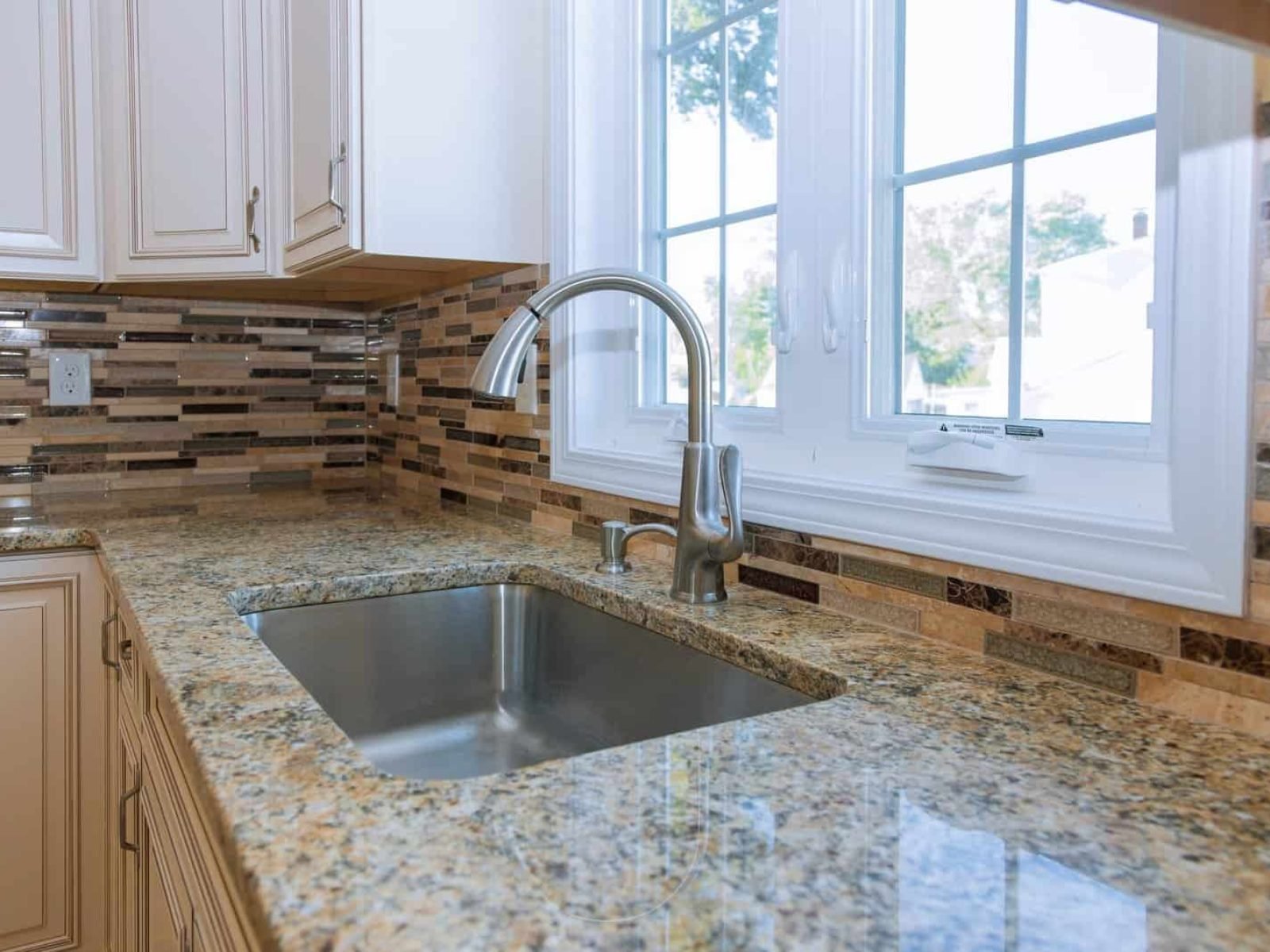 Close-up of granite kitchen countertop with sink and window view.